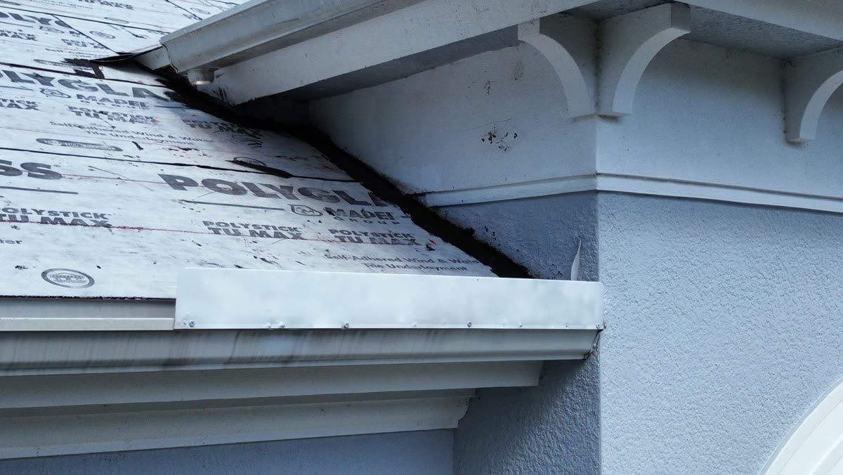Old, worn wall flashing left in place at a roof-to-wall transition during a tear-off, with brand-new underlayment installed around it