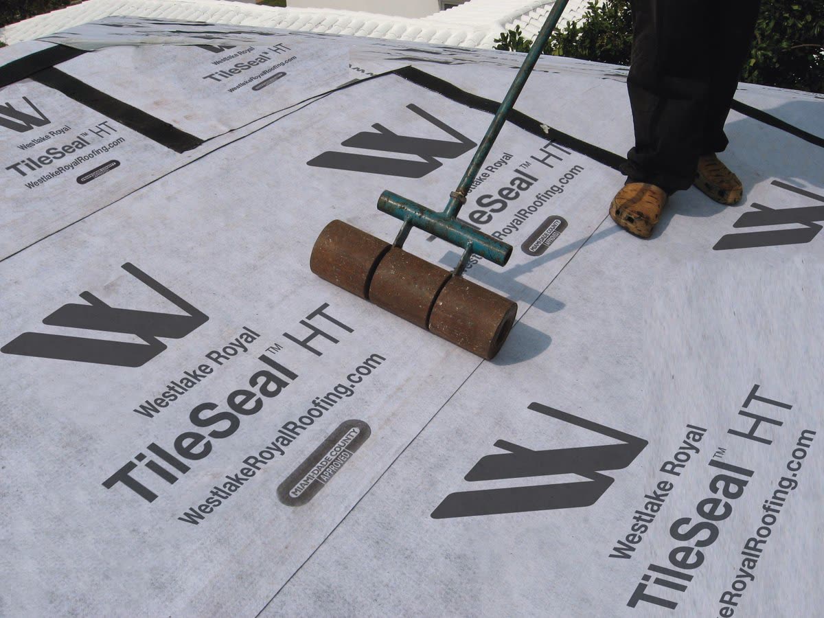 A self-adhered synthetic underlayment being rolled onto roof decking during a tile roof installation